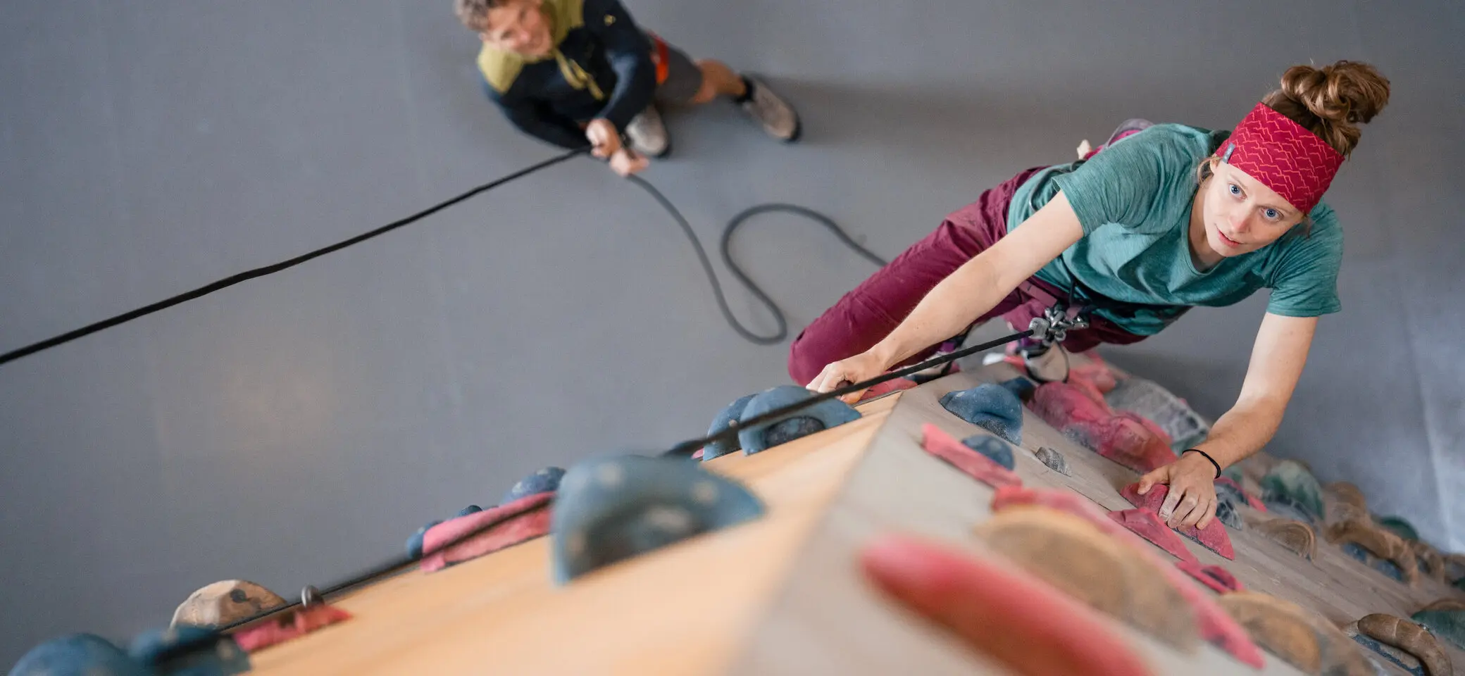 Eine Frau klettert in einer Kletterhalle, ihr Partner sichert sie. | © DAV / Julian Rohn