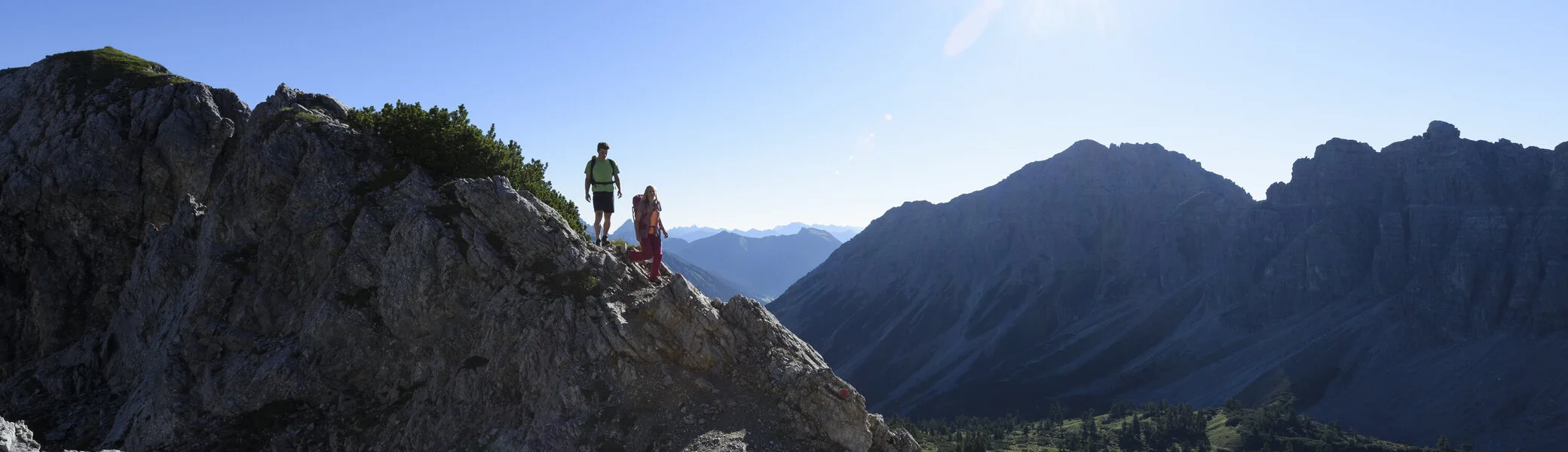 Zwei Wanderer auf einem Felsgrat. Im Hintergrund grüne Bergwiesen | © DAV / Wolfgang Ehn